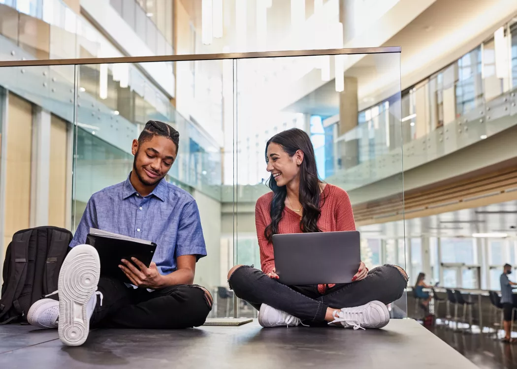 Two students are sitting on the floor while they study and do academic research on the second floor of the Belknap Academic Building.