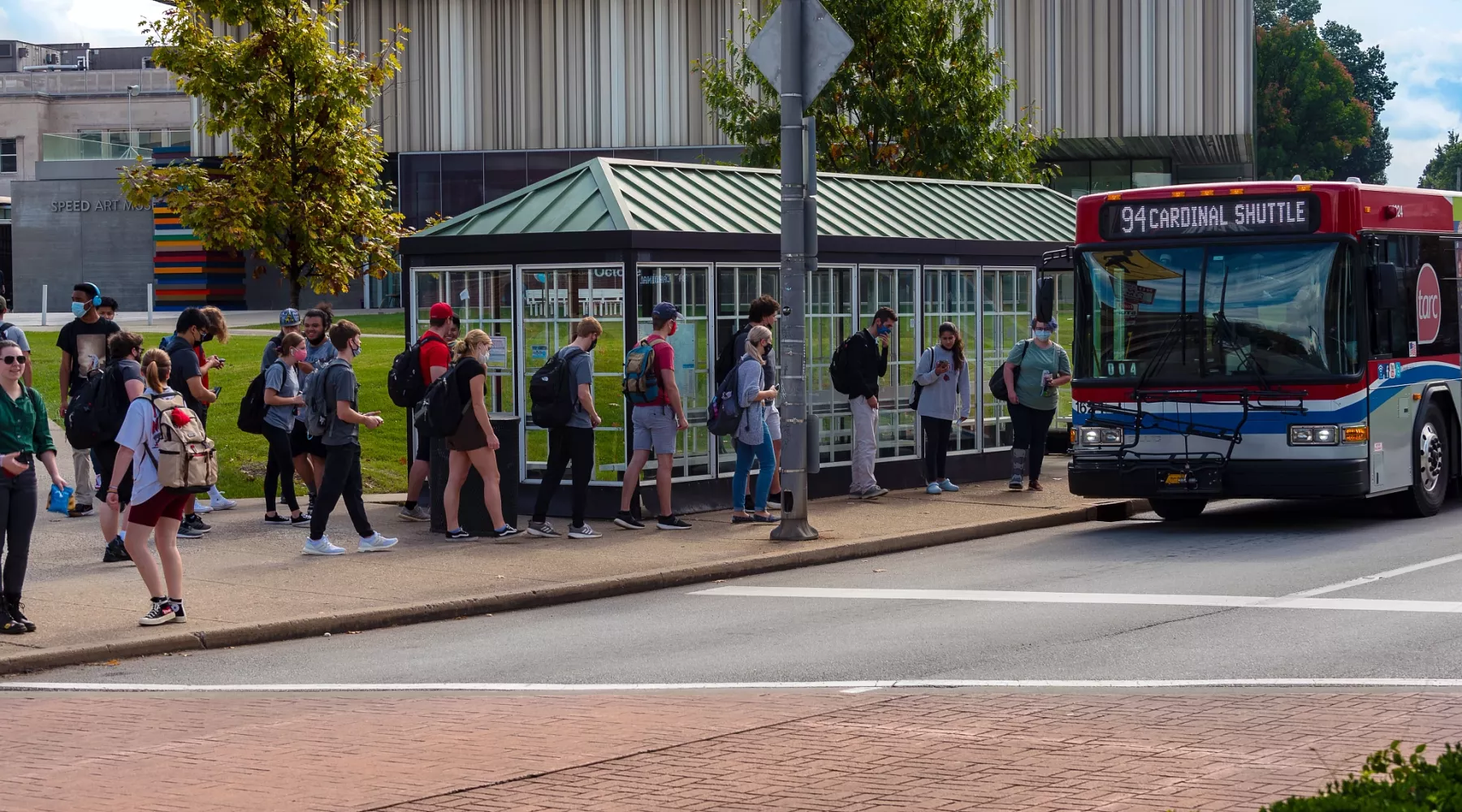 Students waiting for a Cardinal Shuttle with the Speed Art Museum in the background
