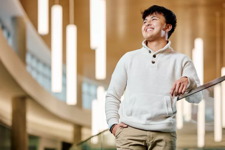 A smiling young male student standing on a modern indoor balcony
