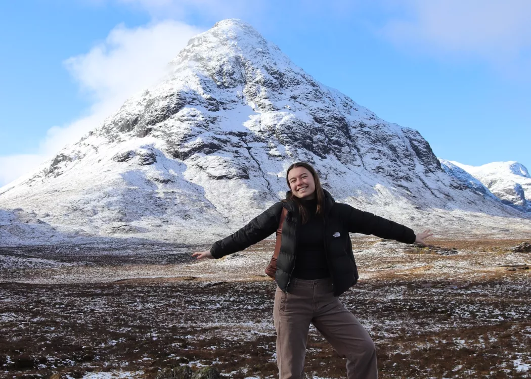 UofL student poses on a rock with a snowy mountain in the background. Scottish Highlands.