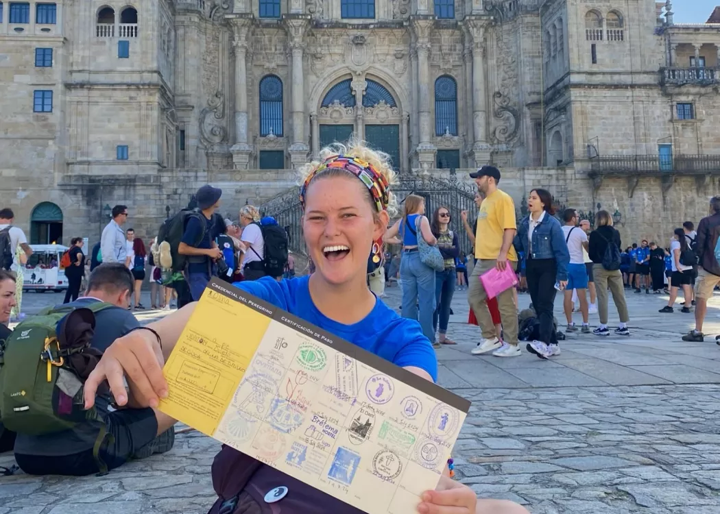 UofL student sits in front of the Santiago Cathedral in Spain smiling and holding a map.