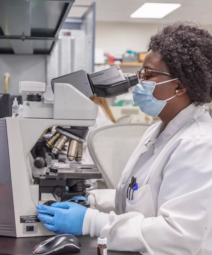 close up woman in white lab coat sitting, looking through microscope