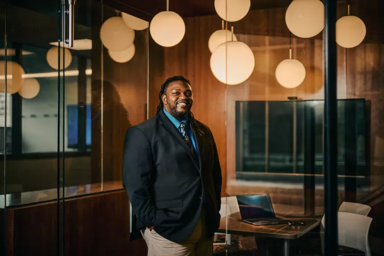 A smiling man in a suit standing in a modern office space.